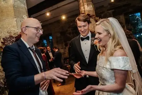 Yorkshire Wedding Magician Adrian Salamon Performing A Magic Trick For A Laughing Bride And Groom During Their Reception. - Hospitium, York